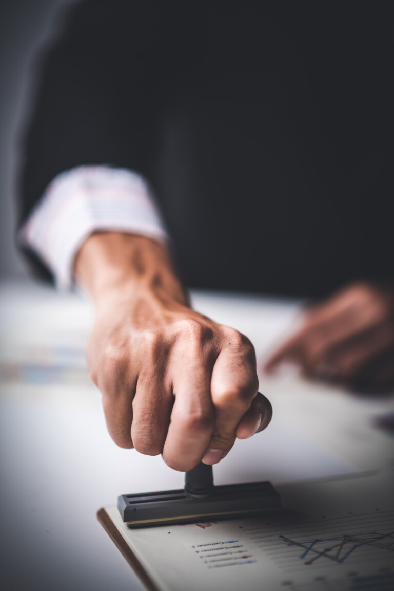 close up of a person's hand stamping with approved stamp on text approved document at desk, contract form paper