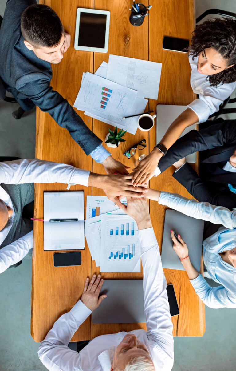 united colleagues holding hands sitting at desk in office, top view